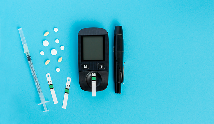 A picture of a blood glucose meter, testing strips, white pills, and an insulin syringe on a light blue background