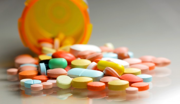 A photo of an orange medication bottle laying on its side, spilling yellow, red, blue, green, and white pills