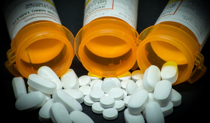 3 pill bottles spilling white pills onto a black background